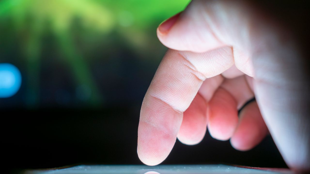 Close-up de um dedo tocando a tela de um smartphone, representando um clique