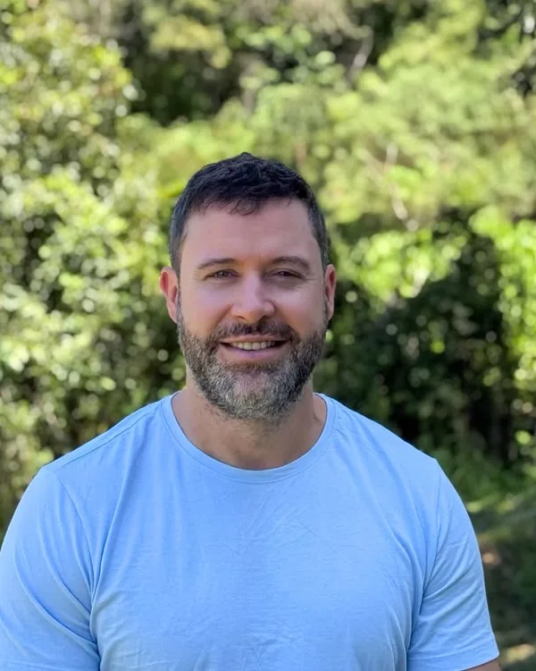 Diego Willian Zietek sorrindo ao ar livre, com árvores ao fundo