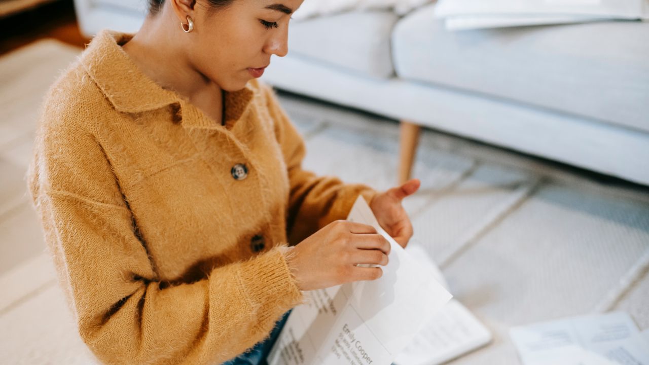 Mulher lendo um documento impresso em casa, atenta ao conteúdo do papel