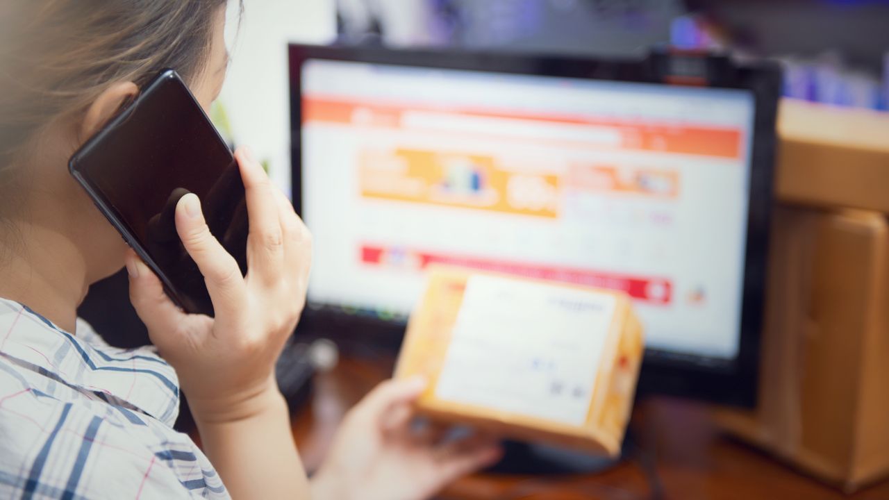 Cliente ao telefone segurando uma caixa de entrega em frente ao computador com loja online aberta