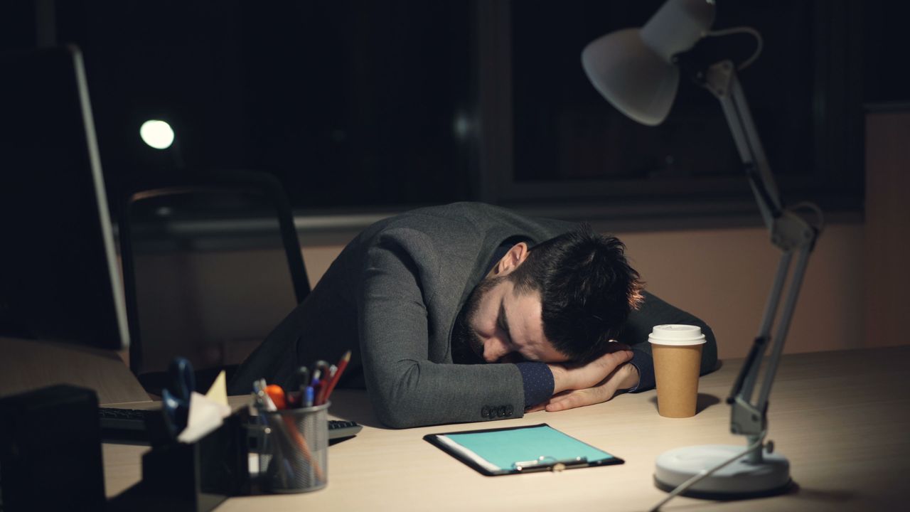 Empresário exausto dormindo sobre a mesa do escritório tarde da noite, ao lado de um café